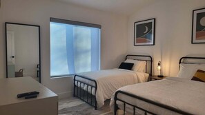 A bedroom with two beds, a desk, a window, and a mirror.