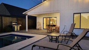 A backyard with a swimming pool, outdoor seating, and a barbecue grill.