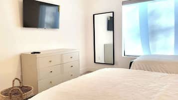 A bedroom with a bed, a dresser, a television, and a window with curtains.