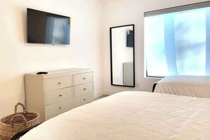 Une chambre à coucher avec un lit, une commode, un téléviseur et une fenêtre avec des rideaux.