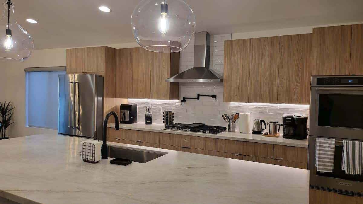 A modern kitchen with stainless steel appliances, wooden cabinets, and pendant lighting.