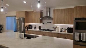 Une cuisine moderne dotée d’appareils électroménagers en acier inoxydable, de meubles en bois et d’un éclairage suspendu.
