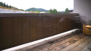 Eine Holzterrasse mit Metallgeländer, einer Holzbank und Blick auf eine hügelige Landschaft.