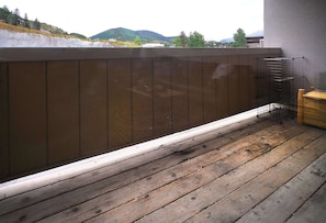 Une terrasse en bois avec une rambarde en métal, un banc en bois et une vue sur un paysage vallonné.