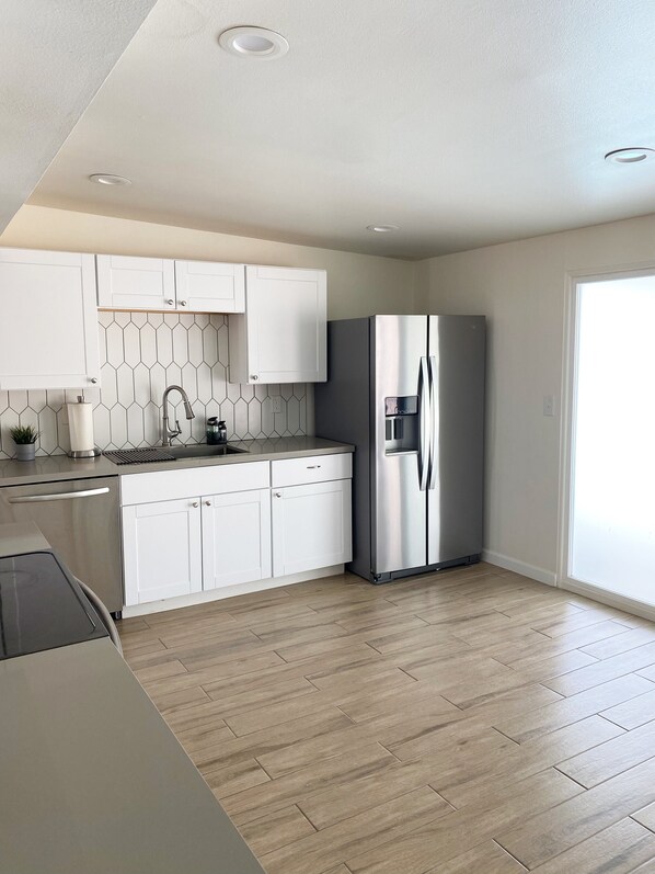 A modern kitchen with white cabinets, a stainless steel refrigerator, and a herringbone-patterned backsplash.