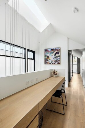 A modern interior with a long wooden desk, a large abstract painting, and a skylight.