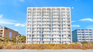 Hotel com vários andares e varandas, situado perto de uma praia.