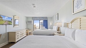 Quarto de hotel com duas camas, cômoda, televisão e varanda com vista.