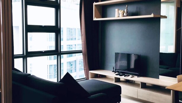 Ein modernes Wohnzimmer mit großem Fenster, einer schwarzen Couch, einem Flachbildfernseher und einem schlichten Regalsystem.