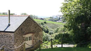 Un bâtiment en pierre doté d’un toit en pente, entouré de verdure et délimité par une barrière en corde.