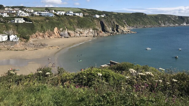 Un paysage côtier avec des maisons sur une colline, une plage de sable et une mer calme.