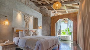 A spacious bedroom with a large bed, a wooden headboard, and a view of a lush garden through a window. - Casa Batu Belig (Keroboken Kelod)