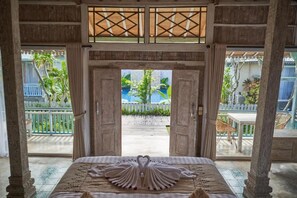 A room with a bed, a view of an outdoor pool, and a balcony with chairs. - Casa Batu Belig (Seminyak)