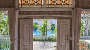 A room with a bed, a woven ceiling light, and a view of a pool and greenery outside. - Casa Batu Belig (Keroboken Kelod)