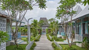 A pathway leading to a traditional-style building with a peaked roof, surrounded by lush greenery and small trees. - Casa Batu Belig (Keroboken Kelod)
