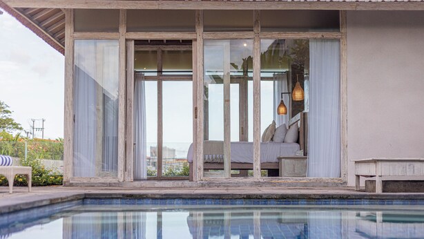 A poolside area with a glass-enclosed bedroom, a bed, and a hanging light fixture. - Casa Batu Belig (Keroboken Kelod)