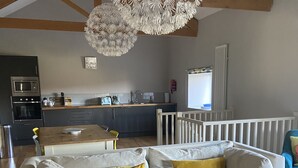A modern living room with a white sofa, yellow cushions, a wooden dining table, and a kitchen in the background. - The Snug - Beautiful Grade 2 listed barn conversion (Mevagissey)