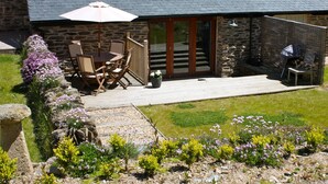 A patio with a table and chairs, a potted plant, and a stone wall. - The Snug - Beautiful Grade 2 listed barn conversion (Mevagissey)
