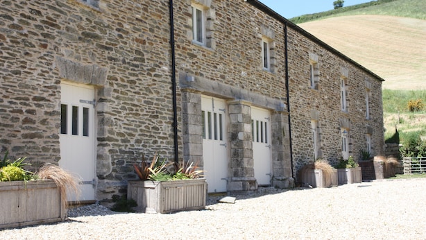 A stone building with multiple doors and windows, surrounded by gravel and plants. - The Snug - Beautiful Grade 2 listed barn conversion (Mevagissey)