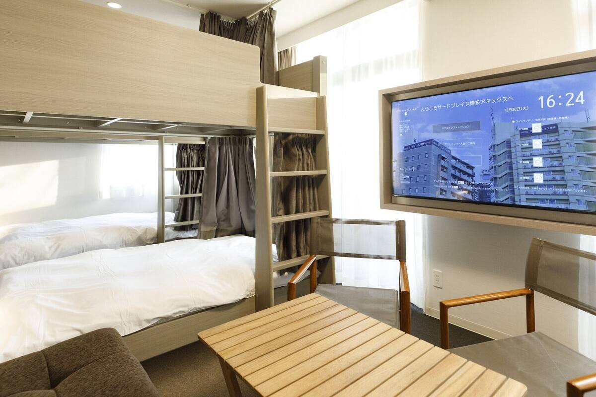 A hotel room with a bunk bed, a desk, and a TV displaying a cityscape.