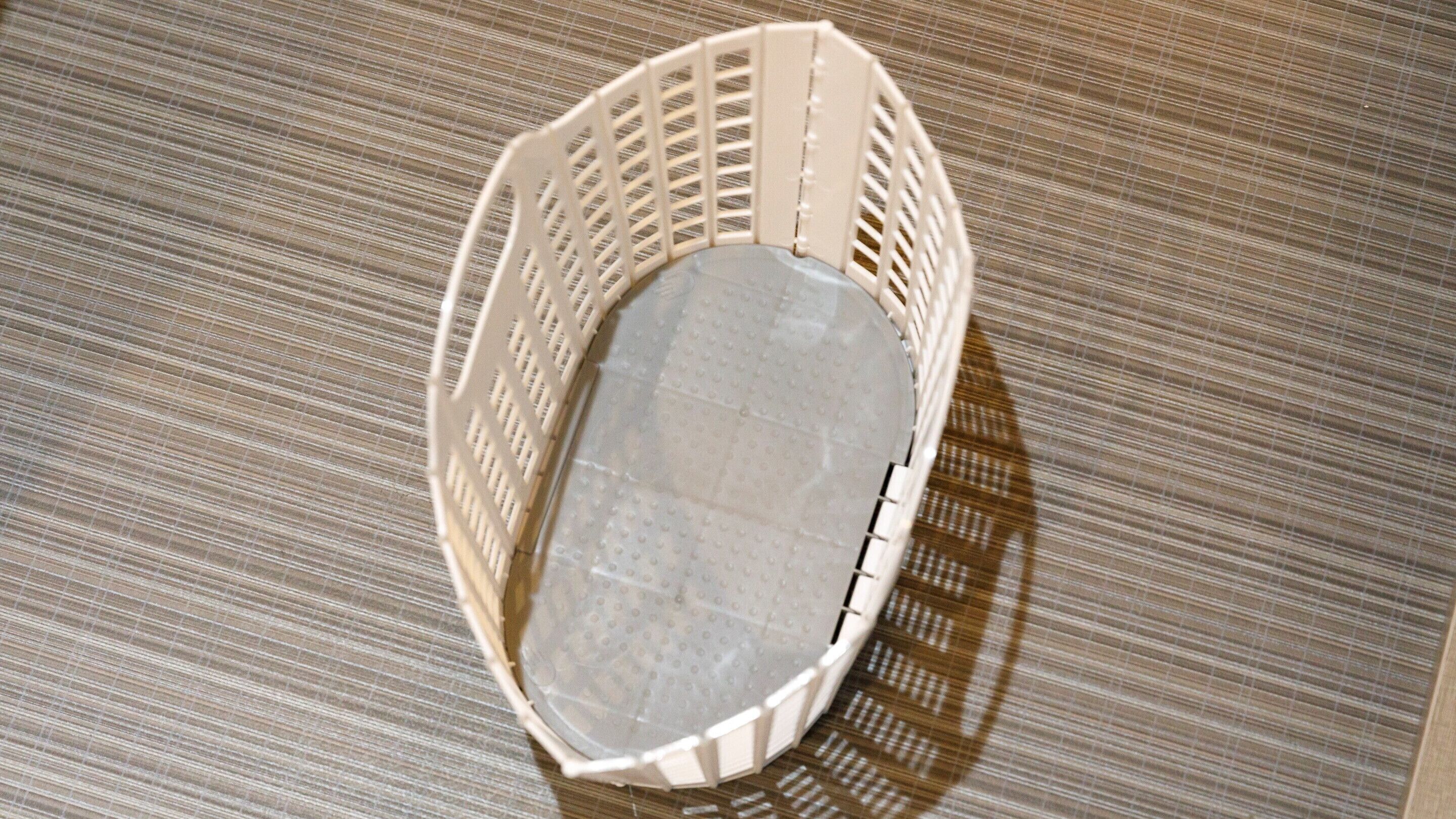 A white plastic basket with a mesh top and a solid bottom, placed on a striped fabric surface.
