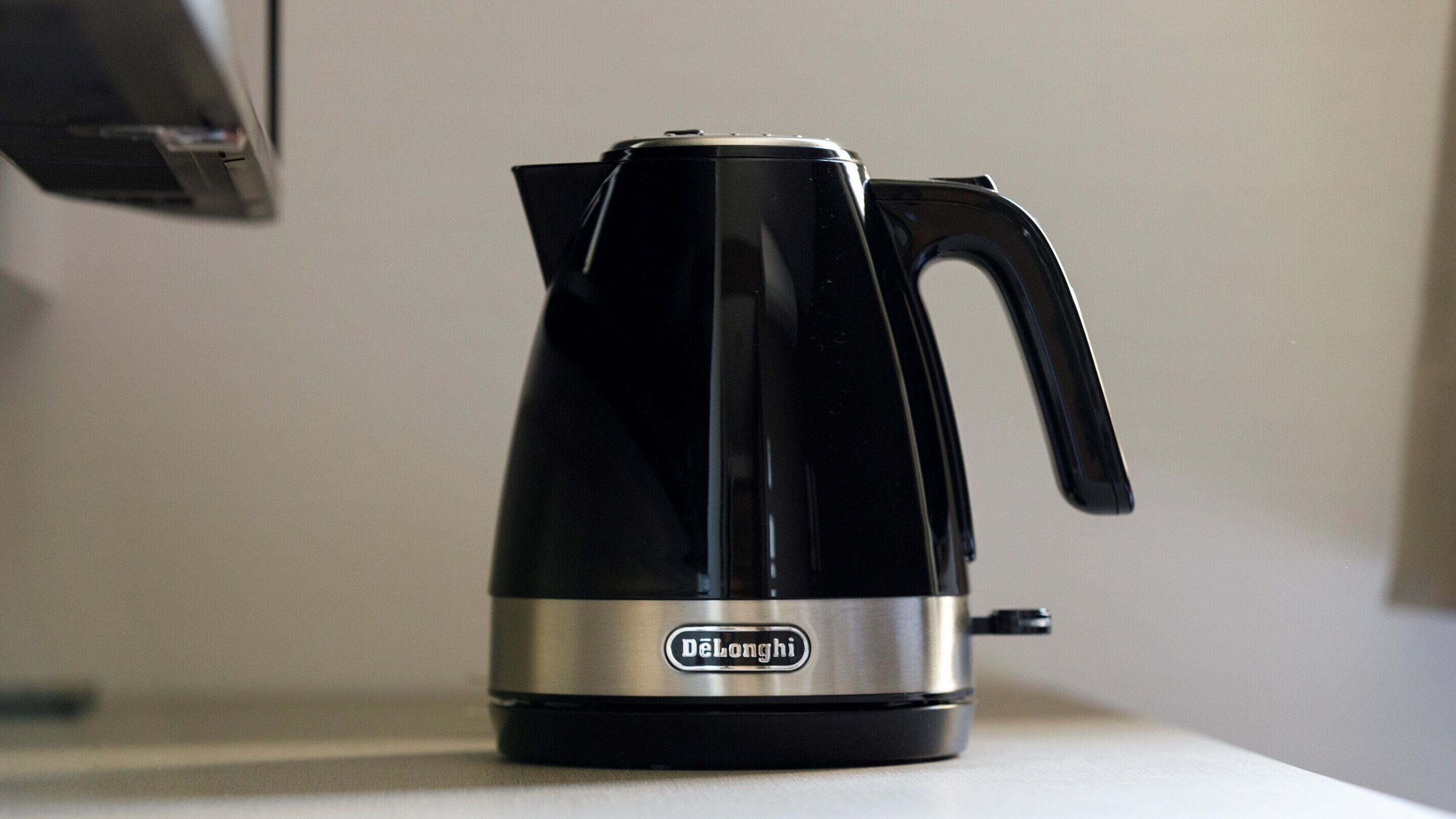 A black and silver DeLonghi electric kettle on a white surface.