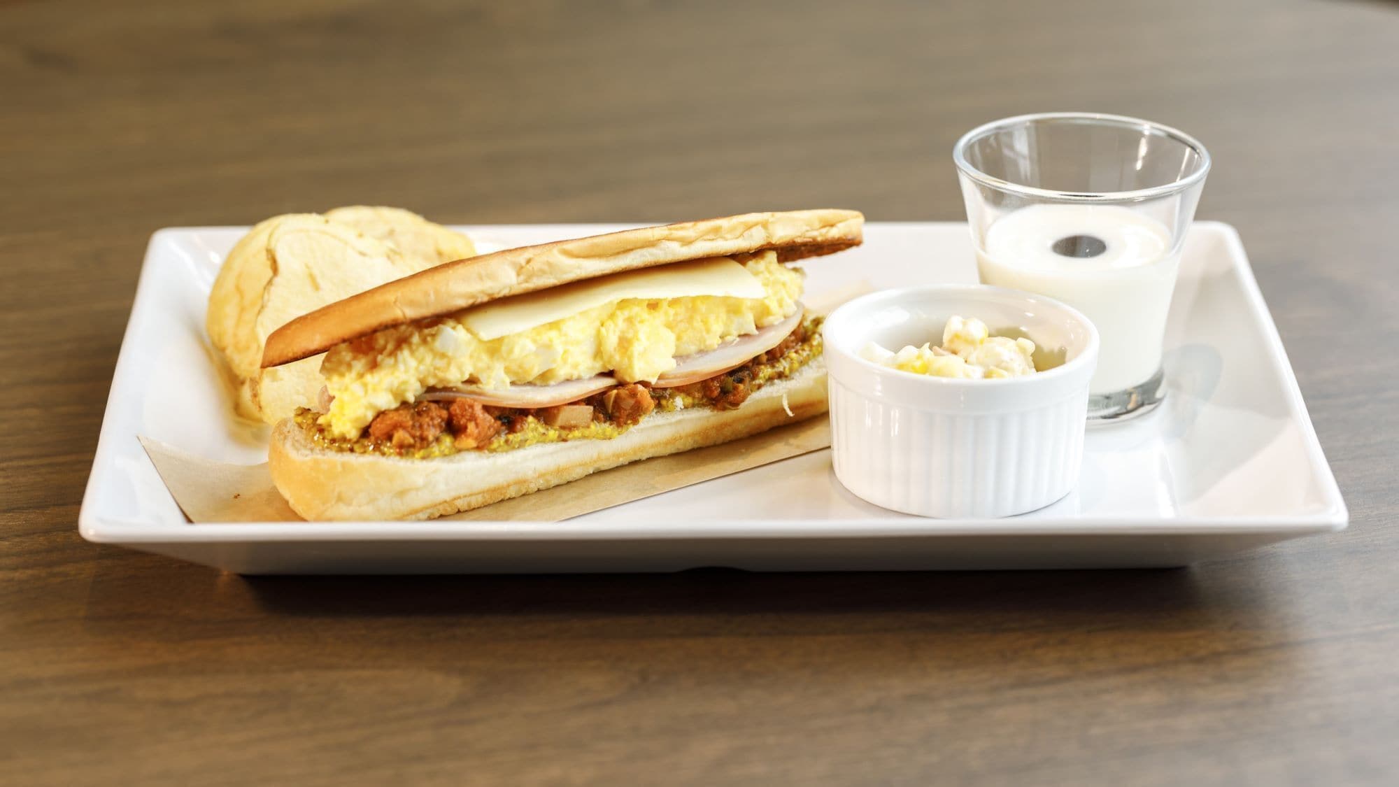 Un sándwich acompañado de salsa y un vaso de leche en una bandeja.