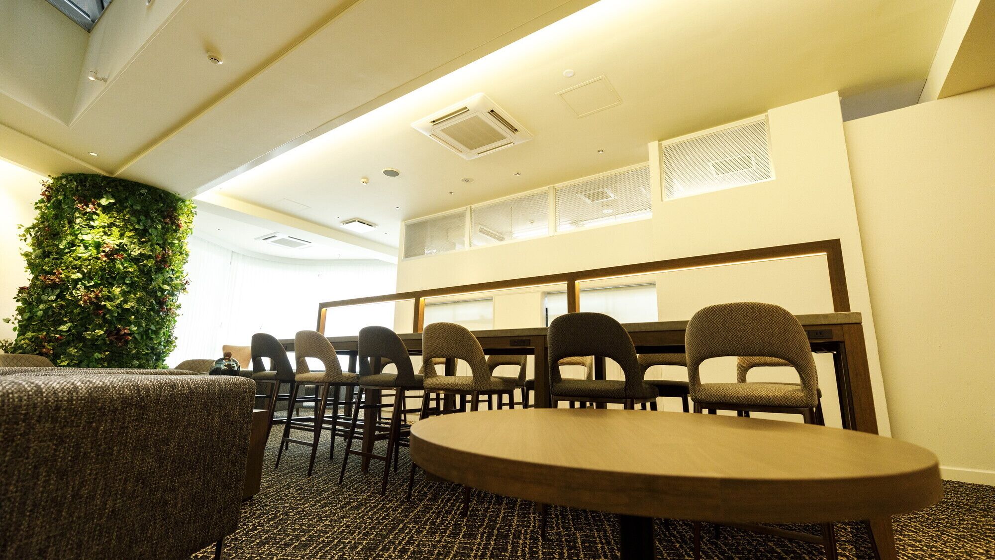 A conference room with a round table, chairs, a green wall, and a ceiling with recessed lighting.
