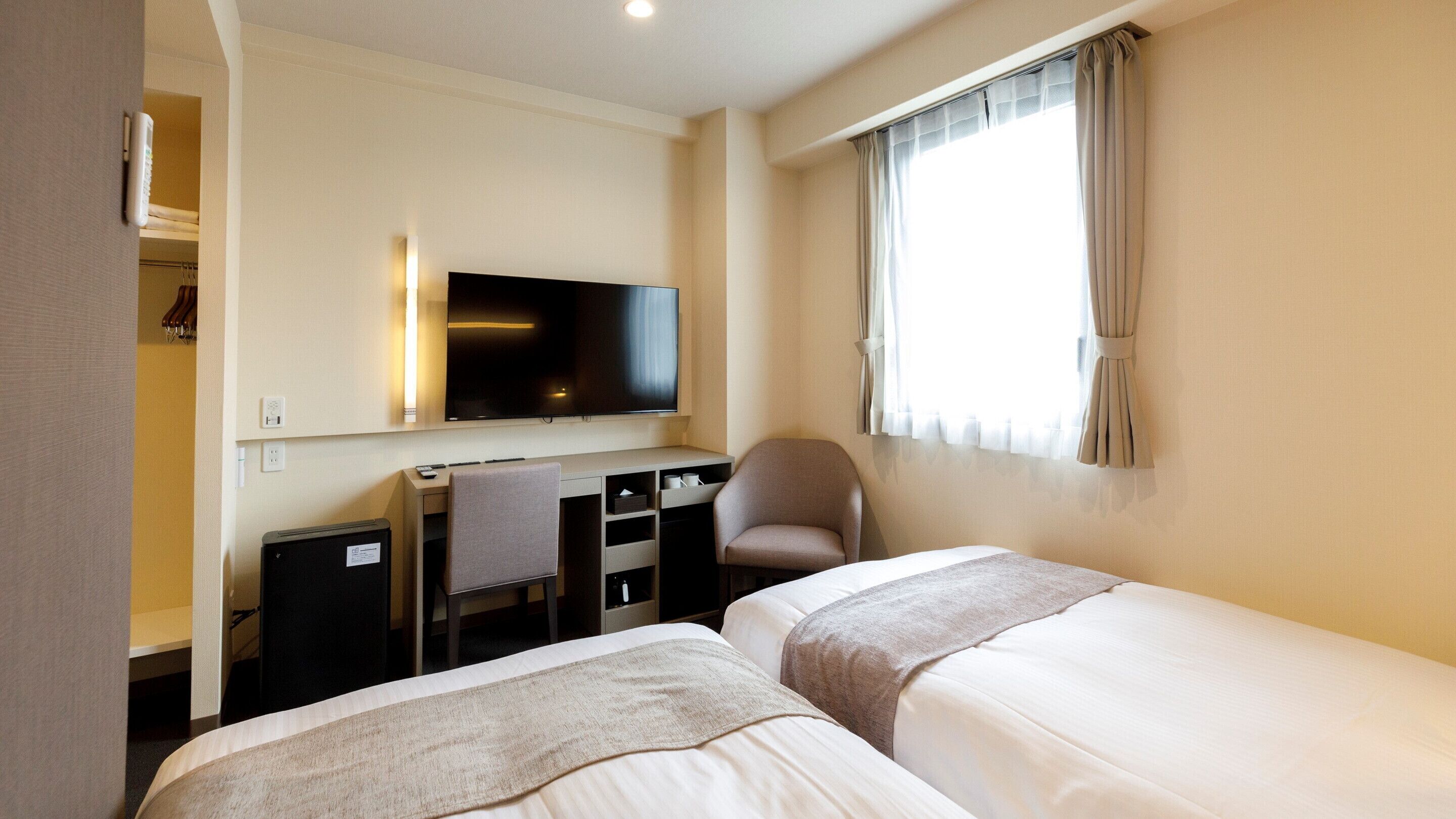 Een hotelkamer met twee bedden, een bureau met stoel, een televisie en een raam met gordijnen.
