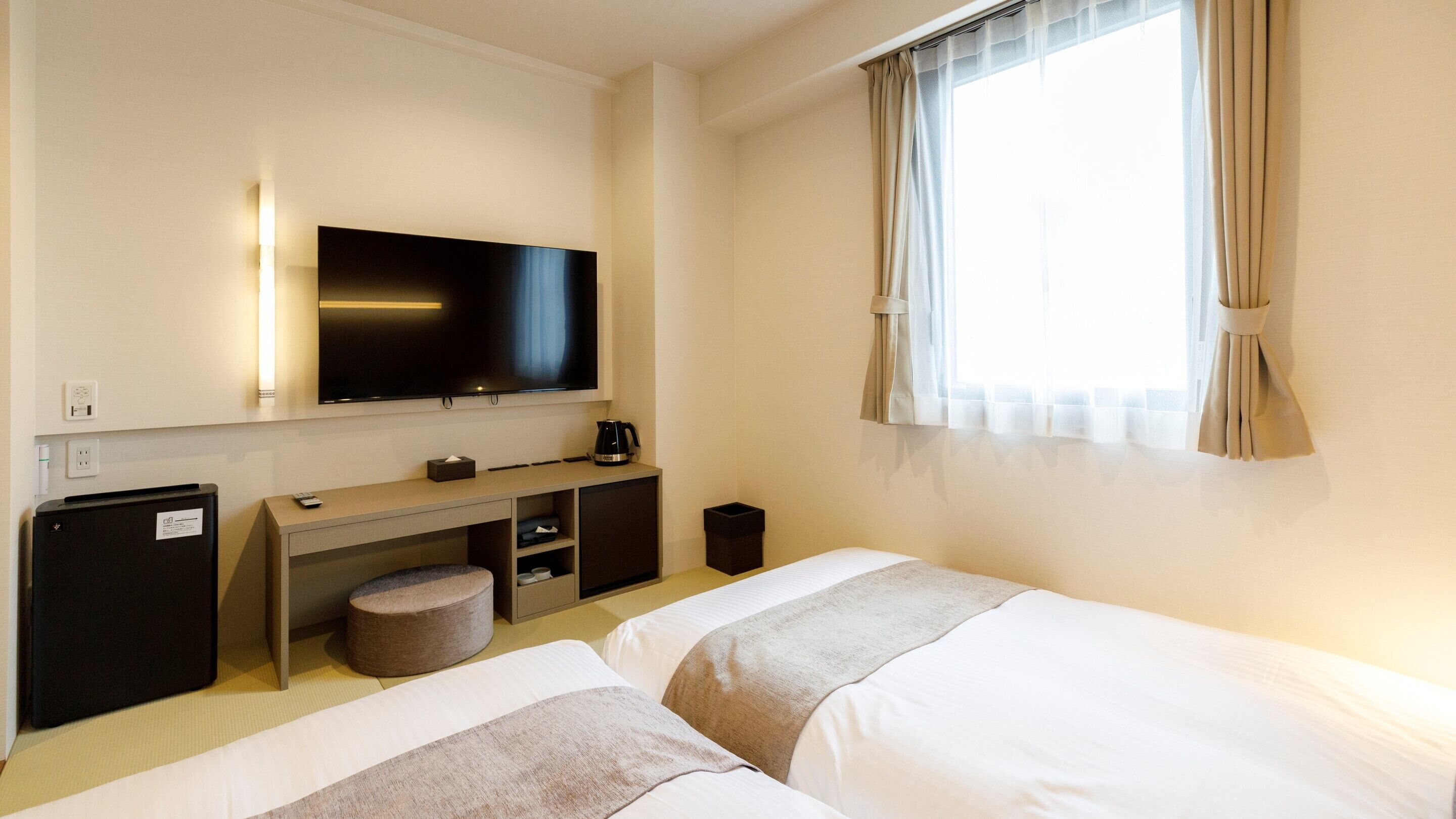 Habitación de hotel con dos camas, televisión, escritorio con cafetera y refrigerador pequeño.