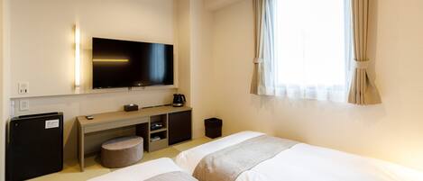 Habitación de hotel con dos camas, televisión, escritorio con cafetera y refrigerador pequeño.