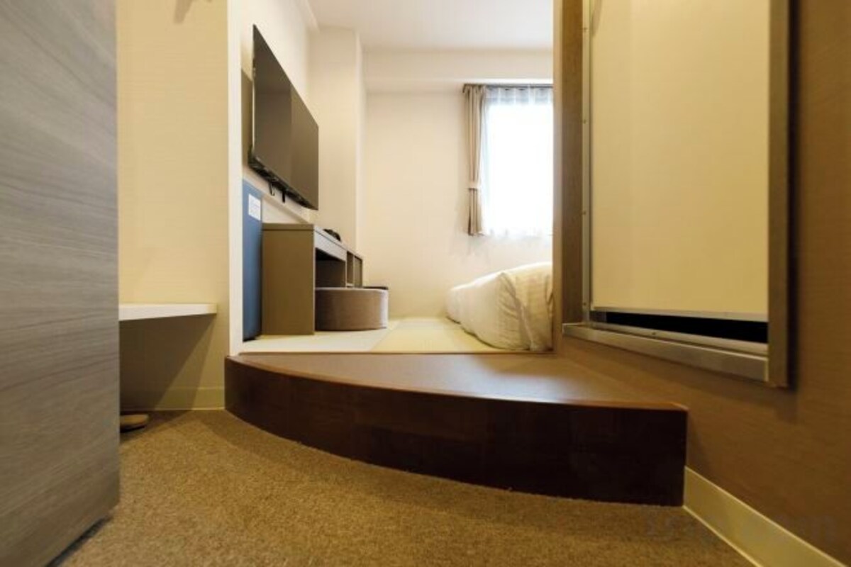 Habitación compacta con banco integrado, televisor de pantalla plana y ventana con cortinas.