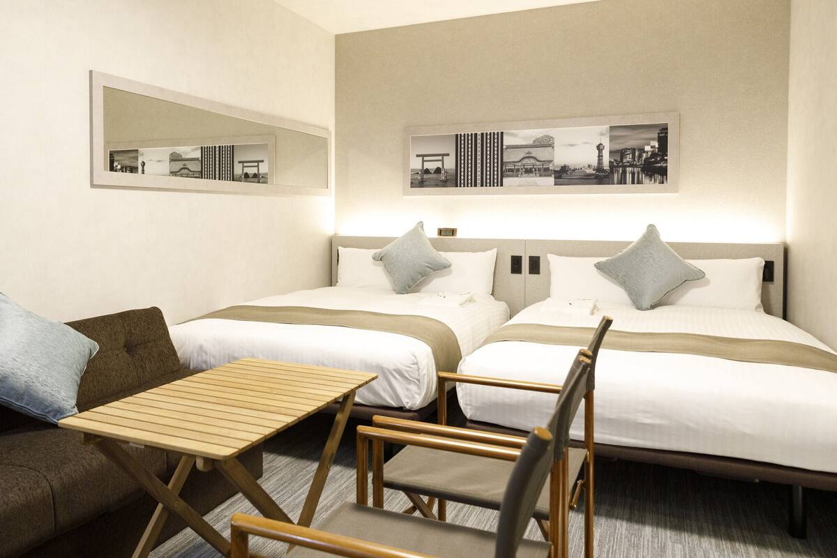A hotel room with two beds, a sofa, a small table, and chairs.