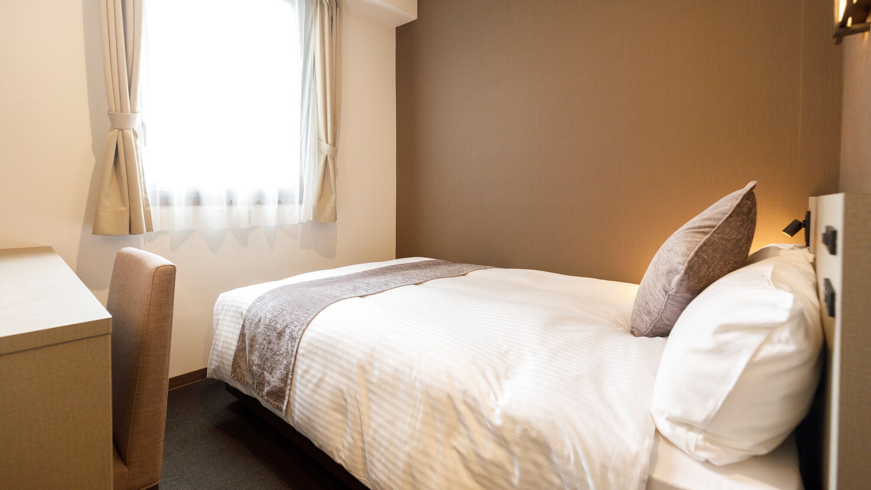 A hotel room with a bed, a desk, and a chair.