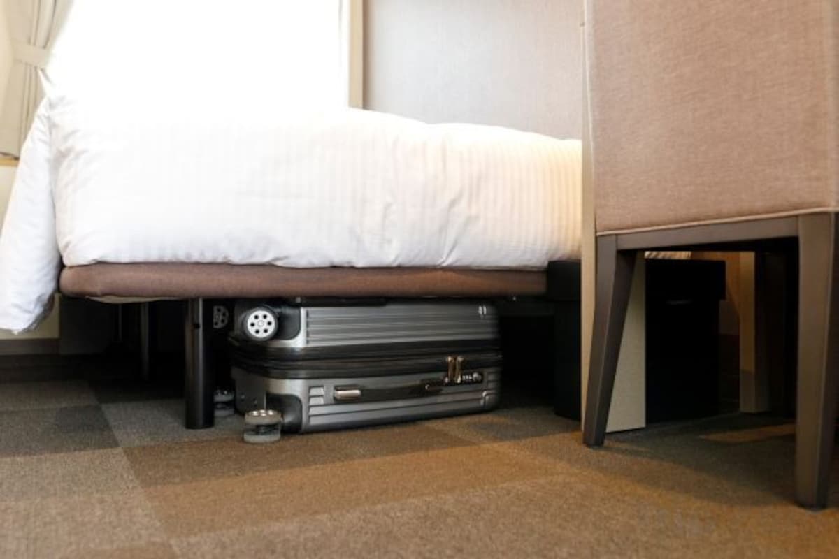 Una cama con una colcha blanca, un banco marrón y una maleta debajo.