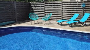 Una piscina con sillas de descanso y una valla de madera al fondo.