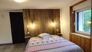 Un dormitorio con cabecera de madera, dos lámparas de noche, una cama grande con colcha estampada y una ventana con vistas a la vegetación.
