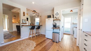 Une cuisine compacte équipée d’un réfrigérateur, d’un four à micro-ondes et d’un petit évier. On y trouve deux tabourets de bar et un plancher en bois.
