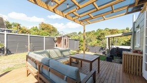 Une terrasse en bois dotée d’un canapé intégré et d’une table, entourée d’une clôture en métal et de verdure.