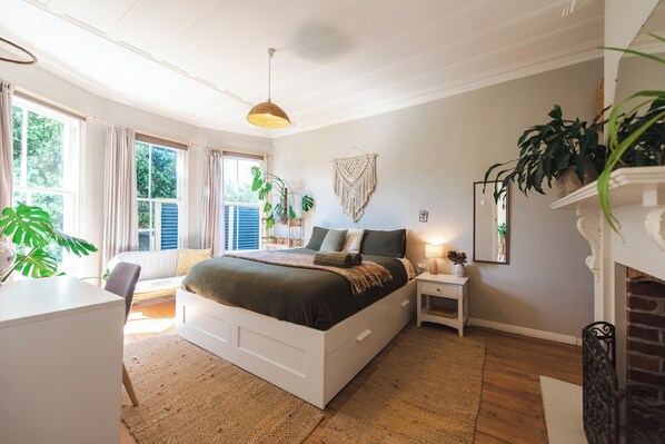Een slaapkamer met een groot bed, nachtkastjes, een bureau en een open haard.