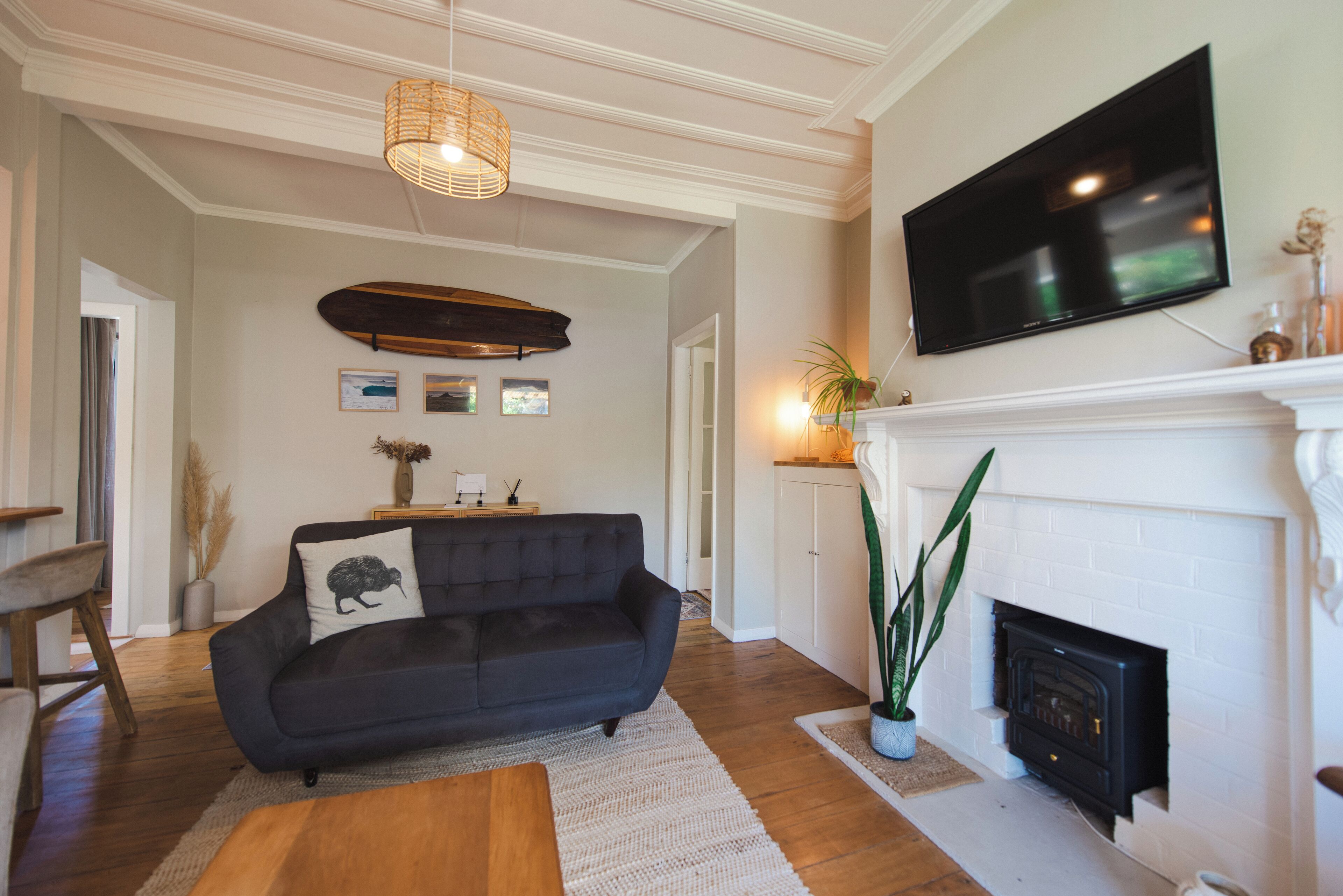 Una sala de estar con un sofá negro, una chimenea, un televisor montado y una lámpara colgante.