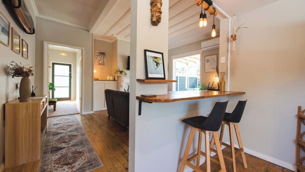Une cuisine moderne avec un bar en bois, deux tabourets de bar noirs et un luminaire suspendu.