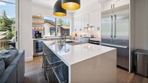 Une cuisine moderne dotée d’un grand îlot central, d’appareils électroménagers en acier inoxydable et de luminaires suspendus.