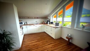 A modern kitchen with white cabinets, wooden flooring, and a large window with a view of greenery. - 5* Lory vacation apartment with castle and panoramic views (Halblech)