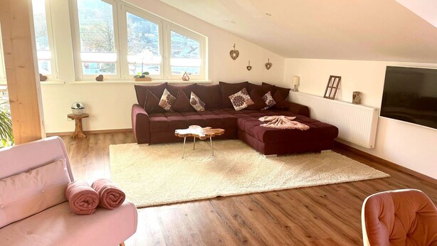 A modern living room with a sectional sofa, a pink armchair, and a wooden coffee table. - 5* Lory vacation apartment with castle and panoramic views (Halblech)