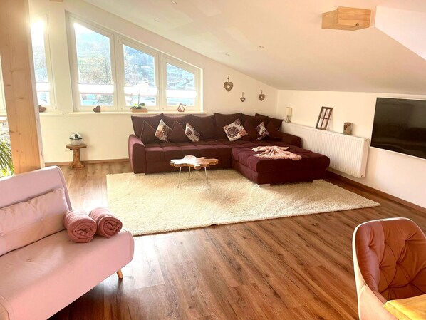 A modern living room with a sectional sofa, a pink armchair, and a wooden coffee table. - 5* Lory vacation apartment with castle and panoramic views (Halblech)