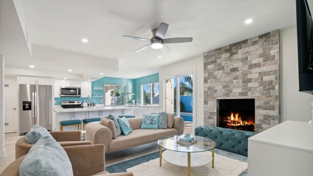 A modern living room with a fireplace, a kitchen with a built-in microwave, and a ceiling fan.