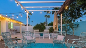 A patio with wicker chairs and a pool, string lights, and palm trees in the background.