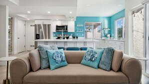 A modern living room with a beige sofa, teal cushions, and a kitchen in the background.