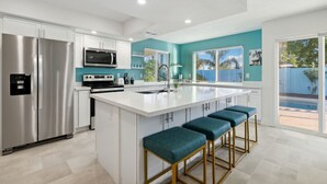 A modern kitchen with a large island, stainless steel appliances, and teal accent walls.